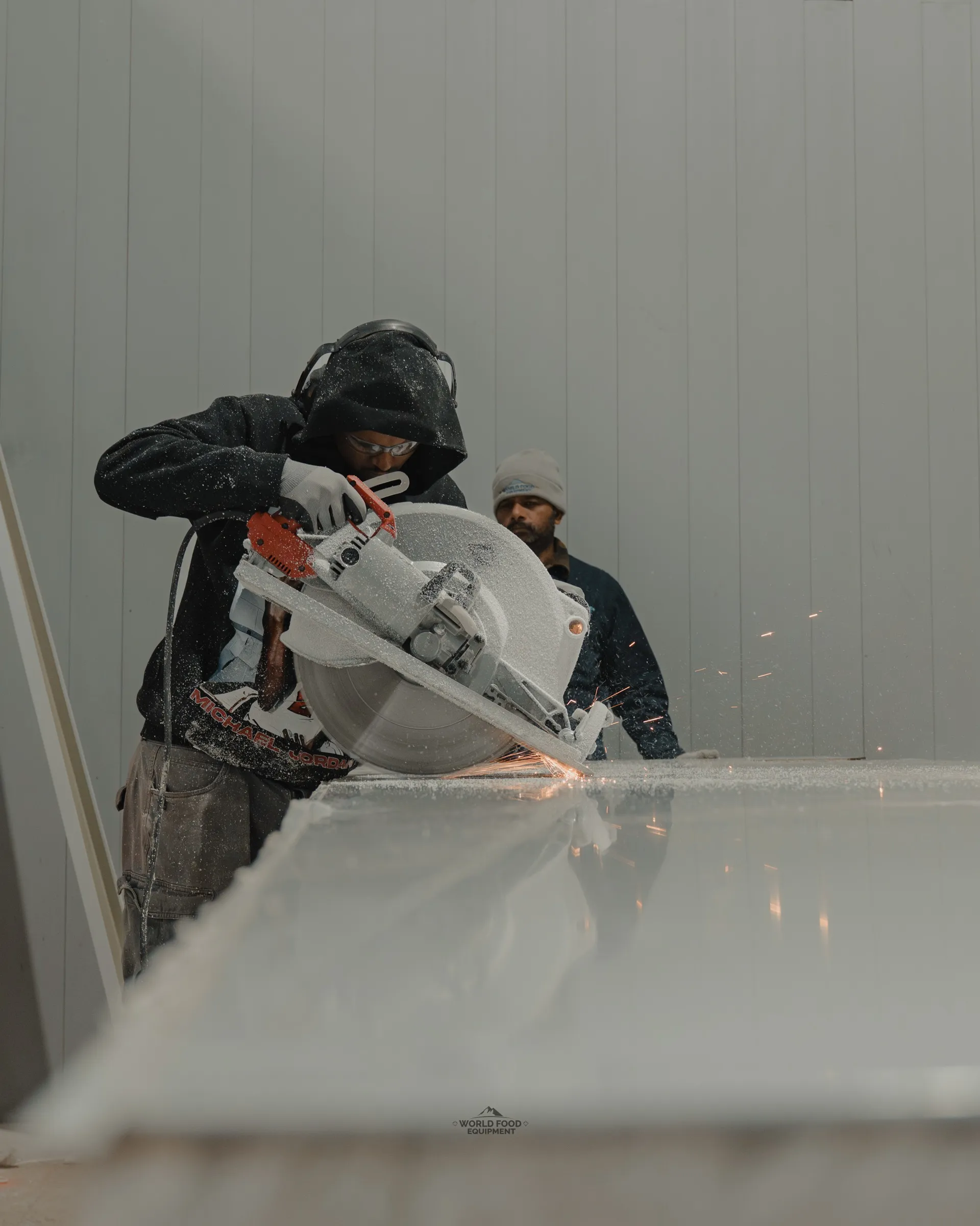 World Food Equipment crew member cutting an insulated cold storage panel on site during the 35 Silton cannabis cultivation build in Ontario, sparks from the saw, white insulated panels staged behind