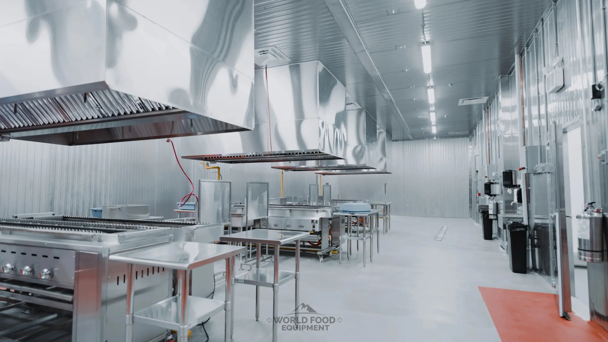 Al Shamas Food Products production room in Mississauga, insulated metal-faced panels on the walls and ceiling, a row of stainless exhaust hoods over the skewer grill line, stainless prep tables, hand-wash stations along the right wall, WFE install.