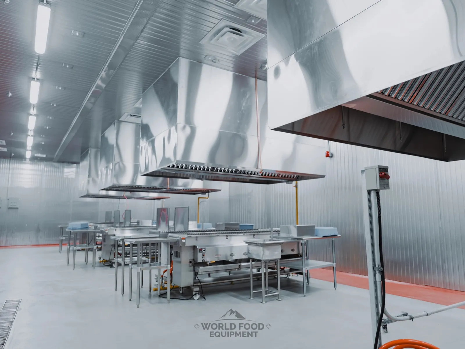 Grill line at Al Shamas Food Products in Mississauga, skewer grills and stainless prep tables under a row of stainless exhaust hoods, insulated panel walls and ceiling, floor trench drain in the foreground, gas drops and electrical disconnects at each station.