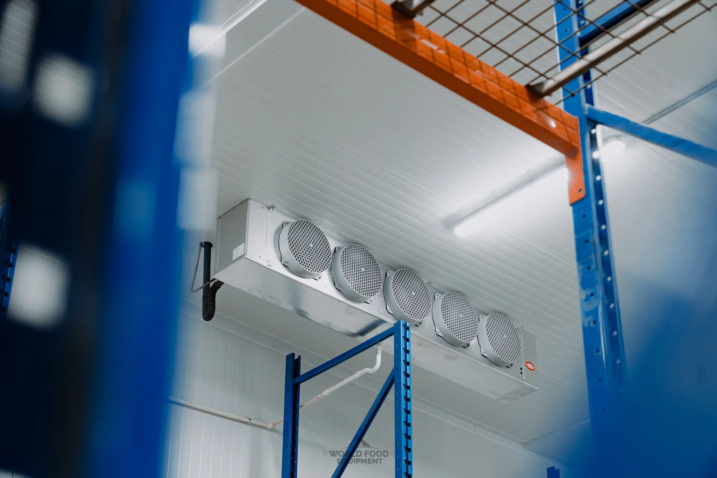 Ceiling-mounted five-fan evaporator unit between blue and orange industrial pallet racking in a finished commercial cold storage facility, Atlas install, Ontario, World Food Equipment.