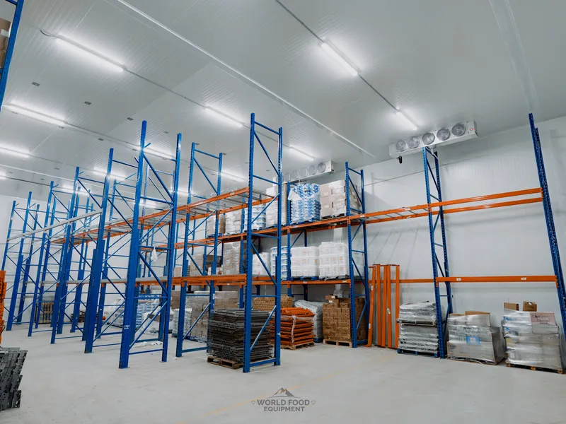 Finished cold-storage room with tall blue-and-orange industrial pallet racking loaded with palletized product, white insulated panel walls, ceiling-mounted evaporators on the back wall, polished concrete floor, Atlas Foods install, Ontario, World Food Equipment