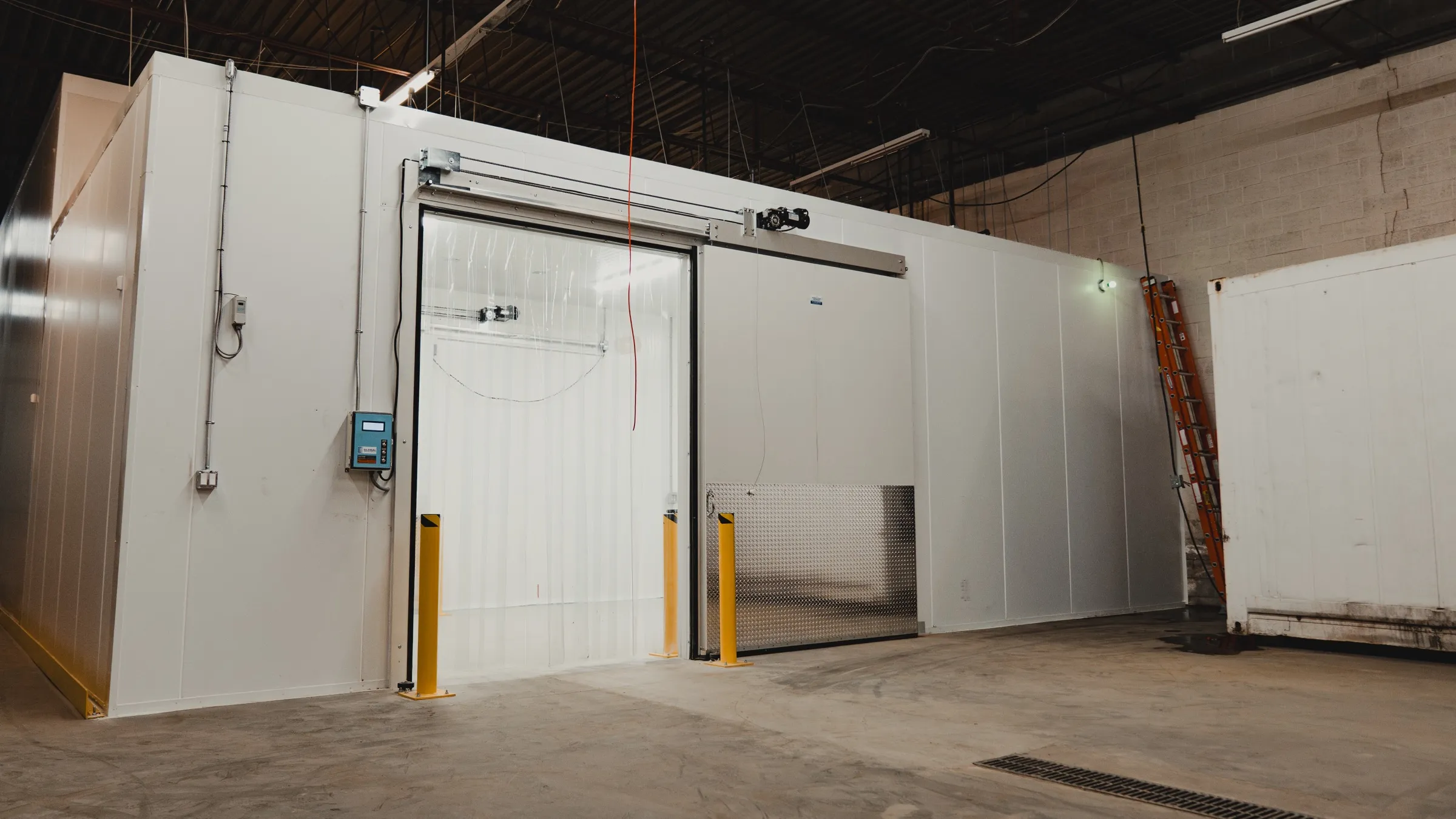 Long finished commercial cold storage room in Ontario with teal pallet racking stocked with product, a KRACK single-fan evaporator on the far wall, bakery racks and boxed goods on the floor, white insulated panel walls and ceiling, SKOR Crestlawn install by World Food Equipment