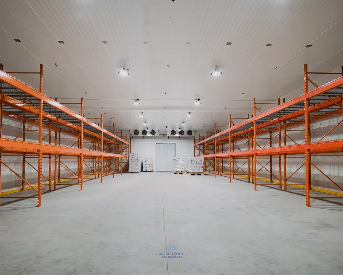 Industrial halal meat processing cold storage warehouse with double-row orange pallet racking down the centre, ceiling-mounted evaporators on the back wall, white insulated panel walls and ceiling, polished concrete floor, Ontario, World Food Equipment