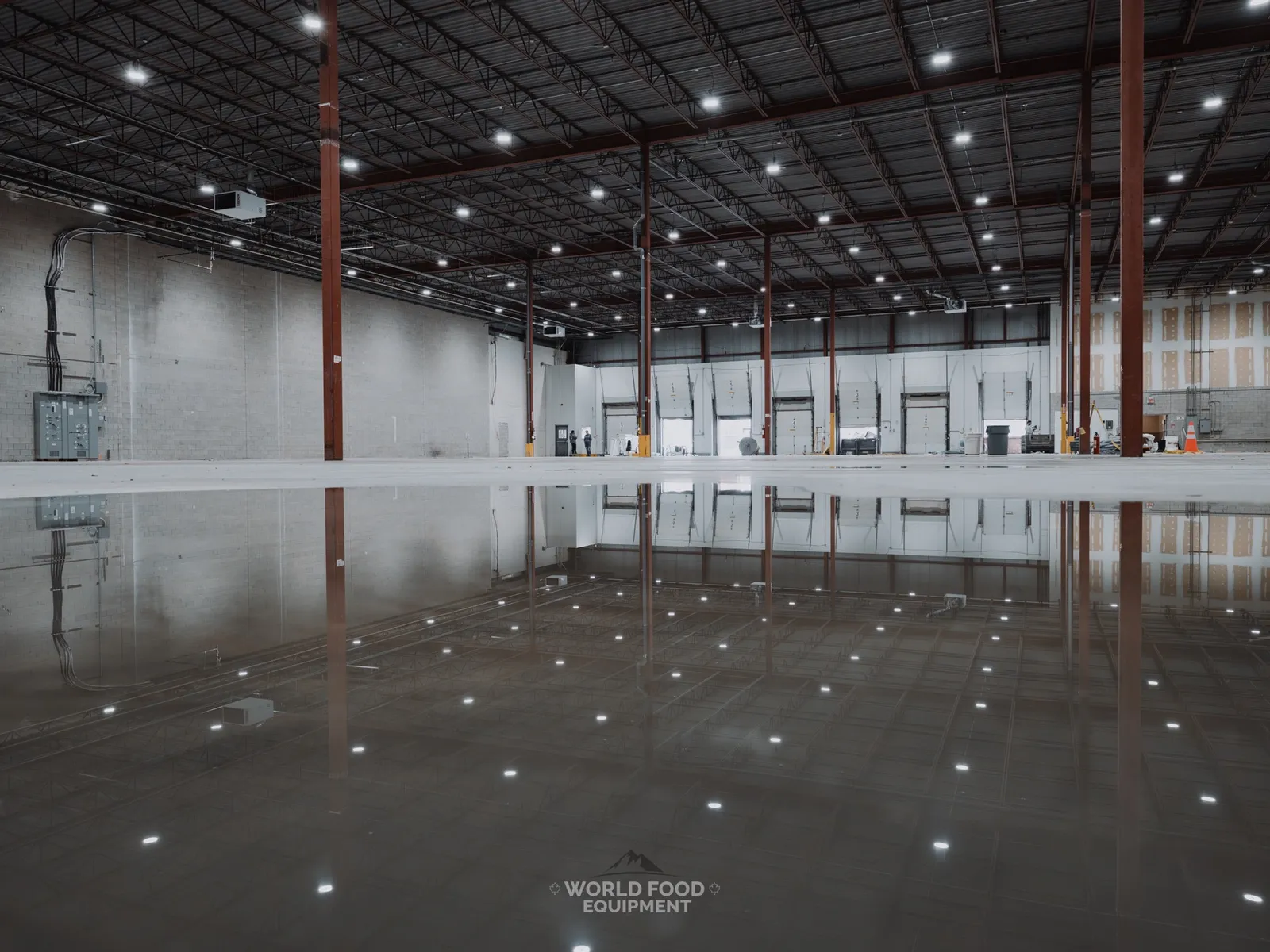 Cleared loading bay area at the Longo's Scarborough site with reflective polished concrete floor mirroring the red structural columns above, full refrigeration plant removed, building structure exposed and clean.