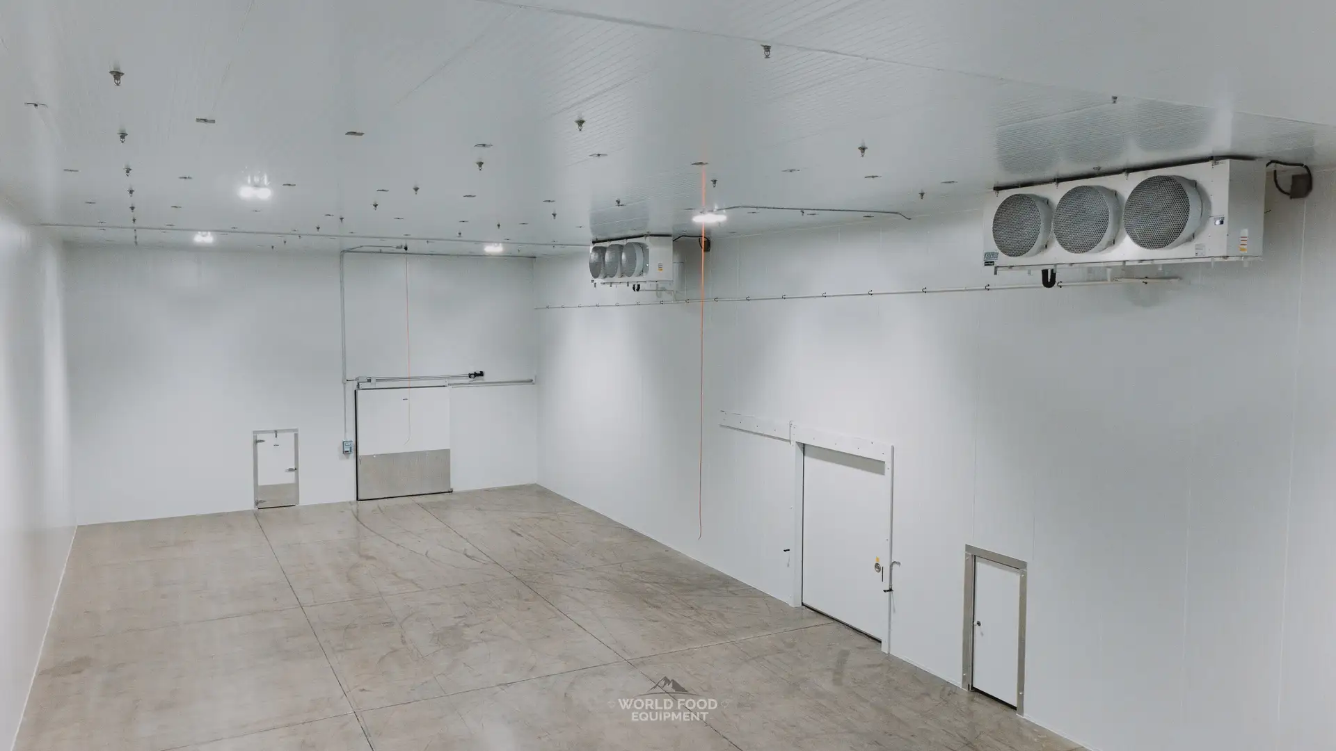 Finished 10,000 sq ft medical-grade cold storage interior at Pacer Air Freight in Mississauga built by World Food Equipment, white insulated panel walls and ceiling, triple-fan KeepRite ceiling evaporators, wide sliding insulated door and swing man doors, sealed concrete floor