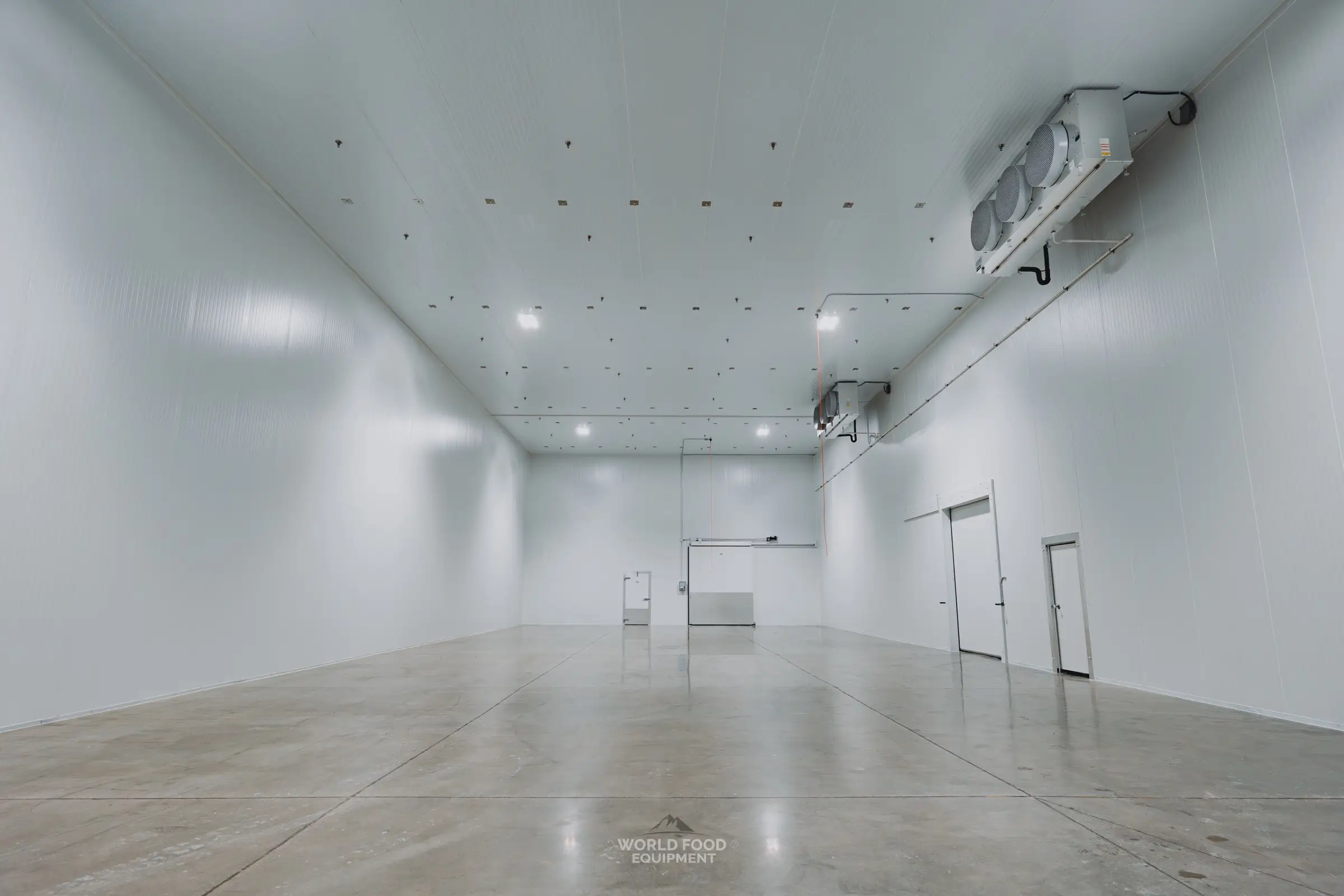 Wide interior of the finished 10,000 sq ft medical-grade cold storage envelope at Pacer Air Freight in Mississauga built by World Food Equipment, white insulated panel walls and ceiling, triple-fan ceiling evaporator, insulated doors at the far wall, sealed concrete floor