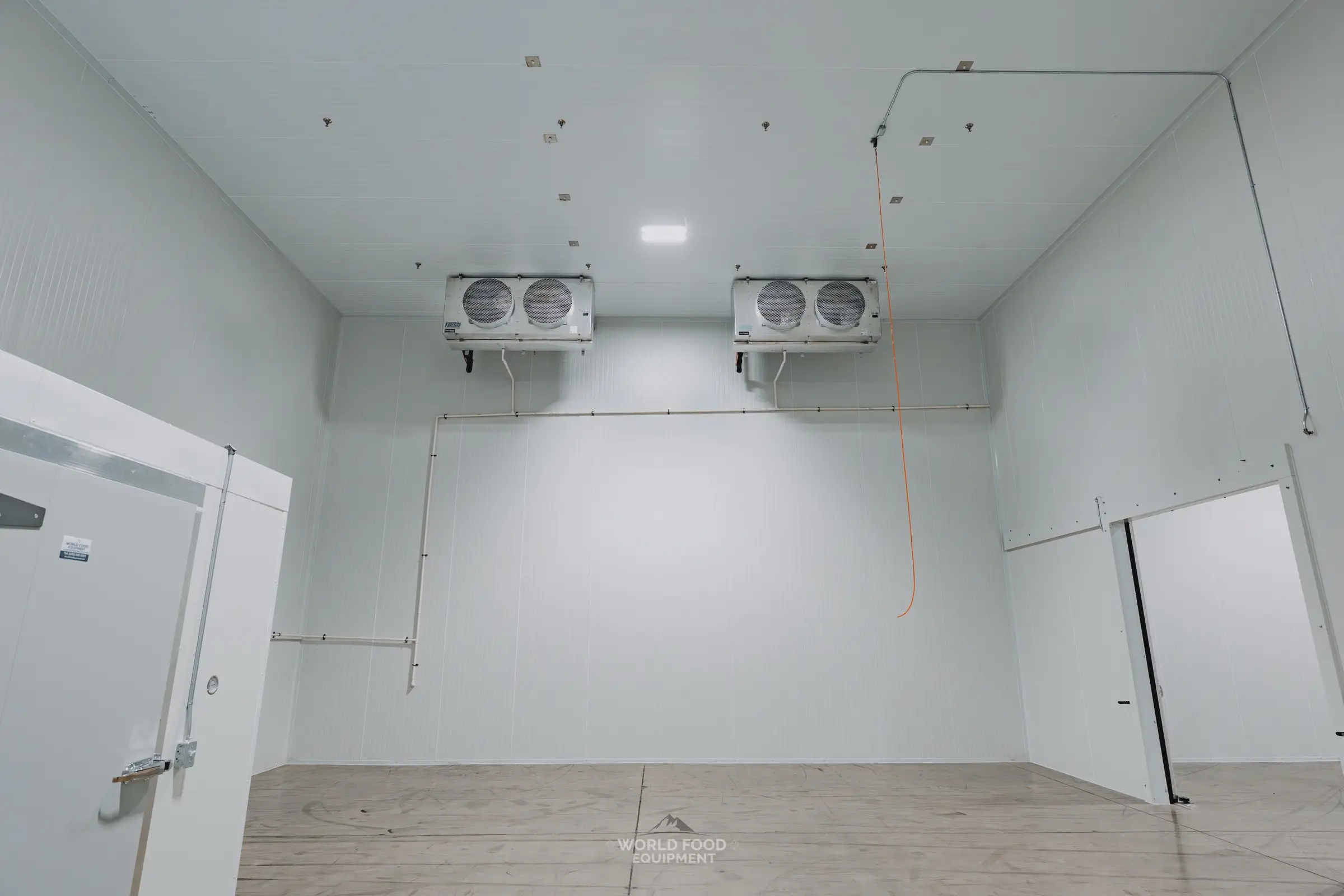 Finished medical-grade cold storage room at Pacer Air Freight in Mississauga: white insulated panel walls, an insulated swing door with a temperature gauge and World Food Equipment decal, a wide sliding insulated door opening, and twin-fan ceiling evaporators