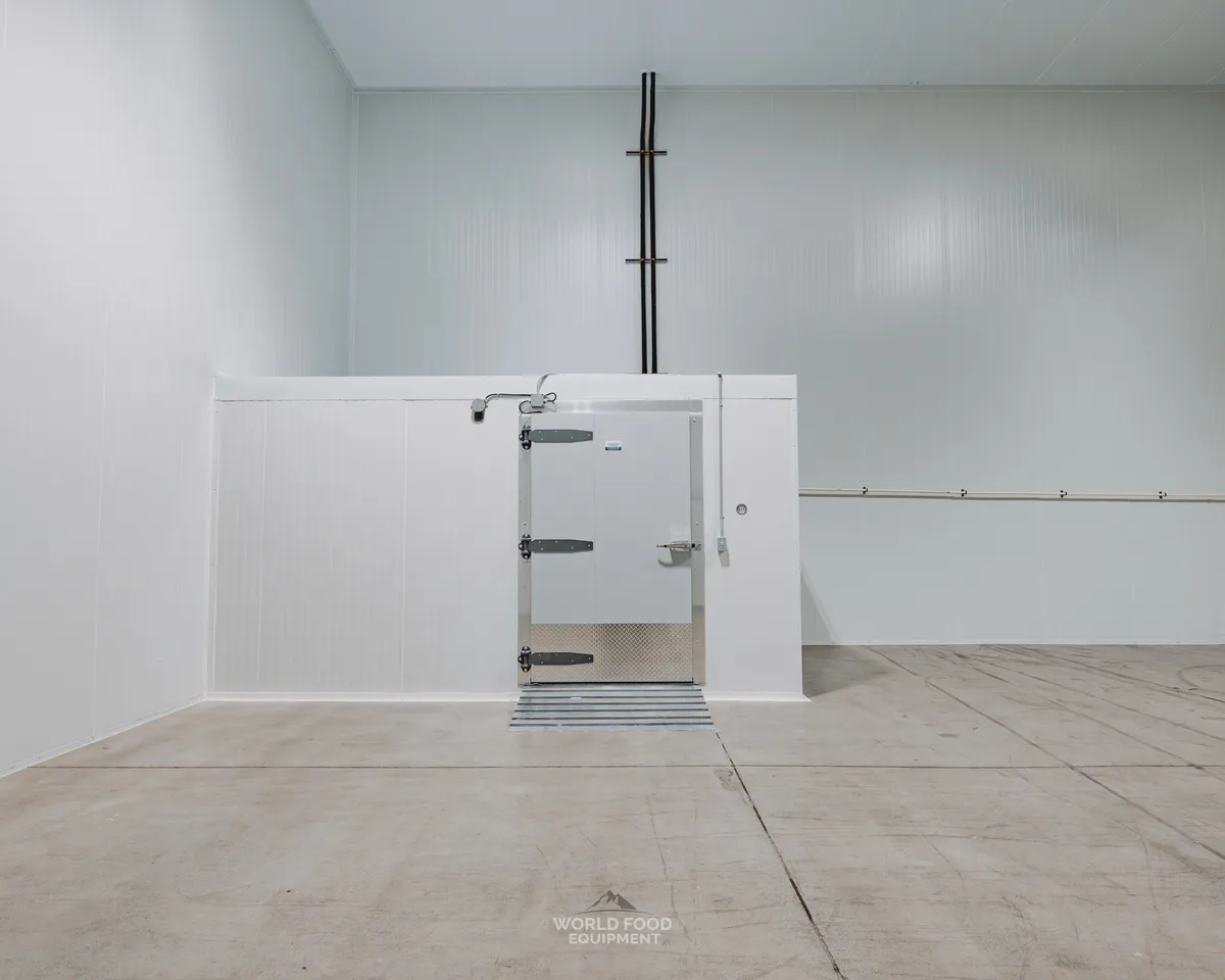 Finished commercial cold storage with a small white insulated swing door set into a box-within-a-box cold room, white insulated panel walls and ceiling, polished concrete floor, Pacer Air Freight install in Mississauga, World Food Equipment