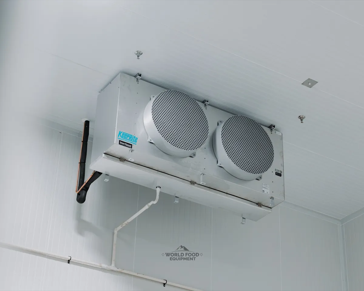 KeepRite SmartSpeed ESP+ twin-fan evaporator ceiling-mounted inside a finished commercial cold storage room, insulated copper refrigerant line set and condensate drain line against white insulated panels, Ontario commercial refrigeration installed by World Food Equipment