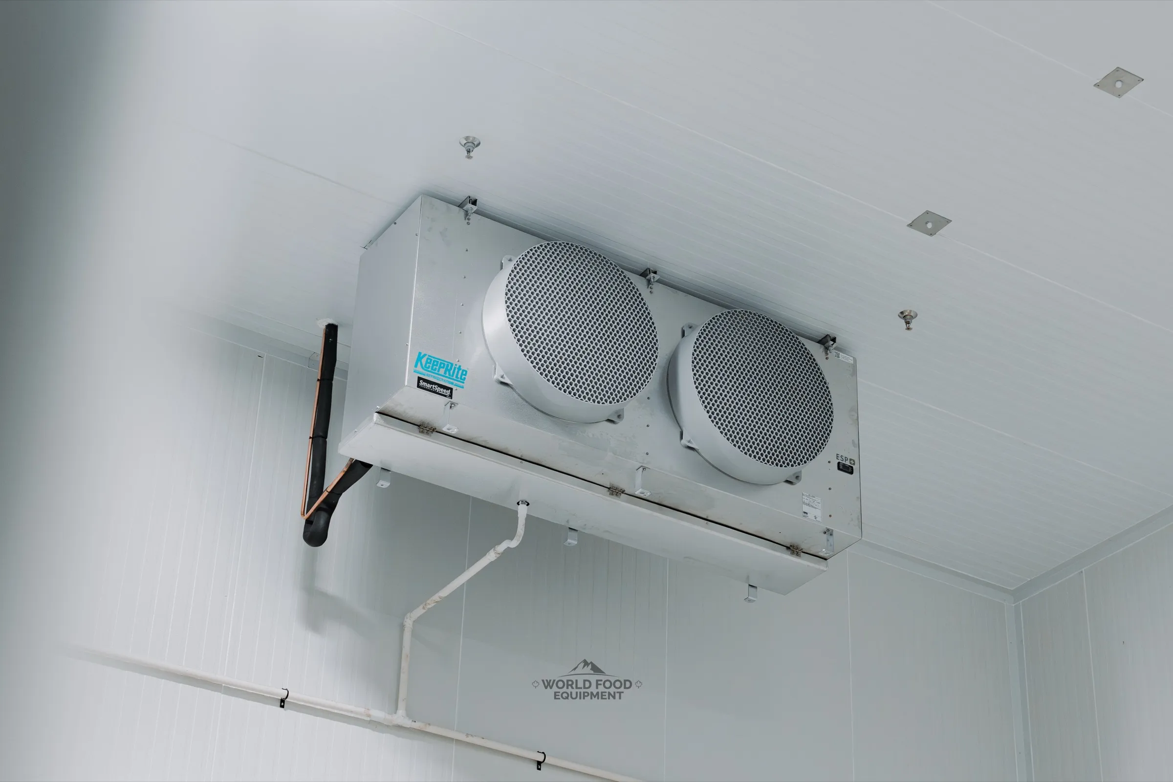 KeepRite SmartSpeed ESP+ twin-fan evaporator ceiling-mounted in the finished medical-grade cold storage at Pacer Air Freight in Mississauga, insulated copper refrigerant line set and condensate drain line, white insulated panels, World Food Equipment install