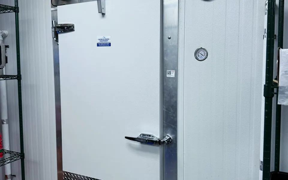 White insulated walk-in cooler swing door with Kason hinges and latch, aluminium frame, diamond-plate kickplate, and a World Food Equipment plate on the door, Ontario install