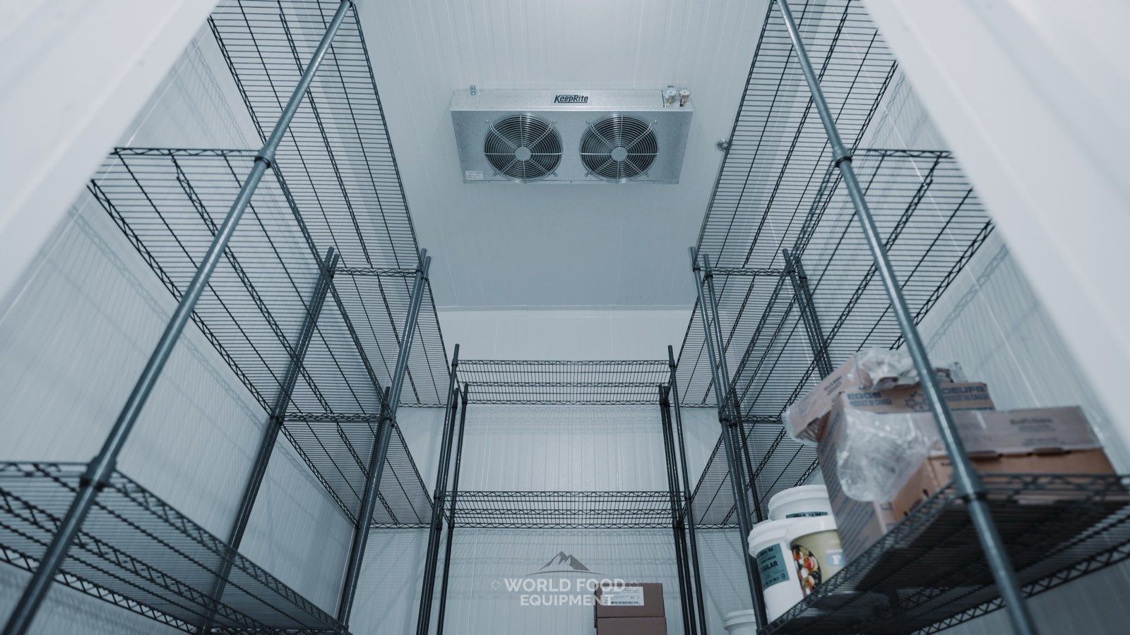 Interior of a WFE-installed walk-in cooler showing a KeepRite dual-fan ceiling evaporator above stocked wire shelving