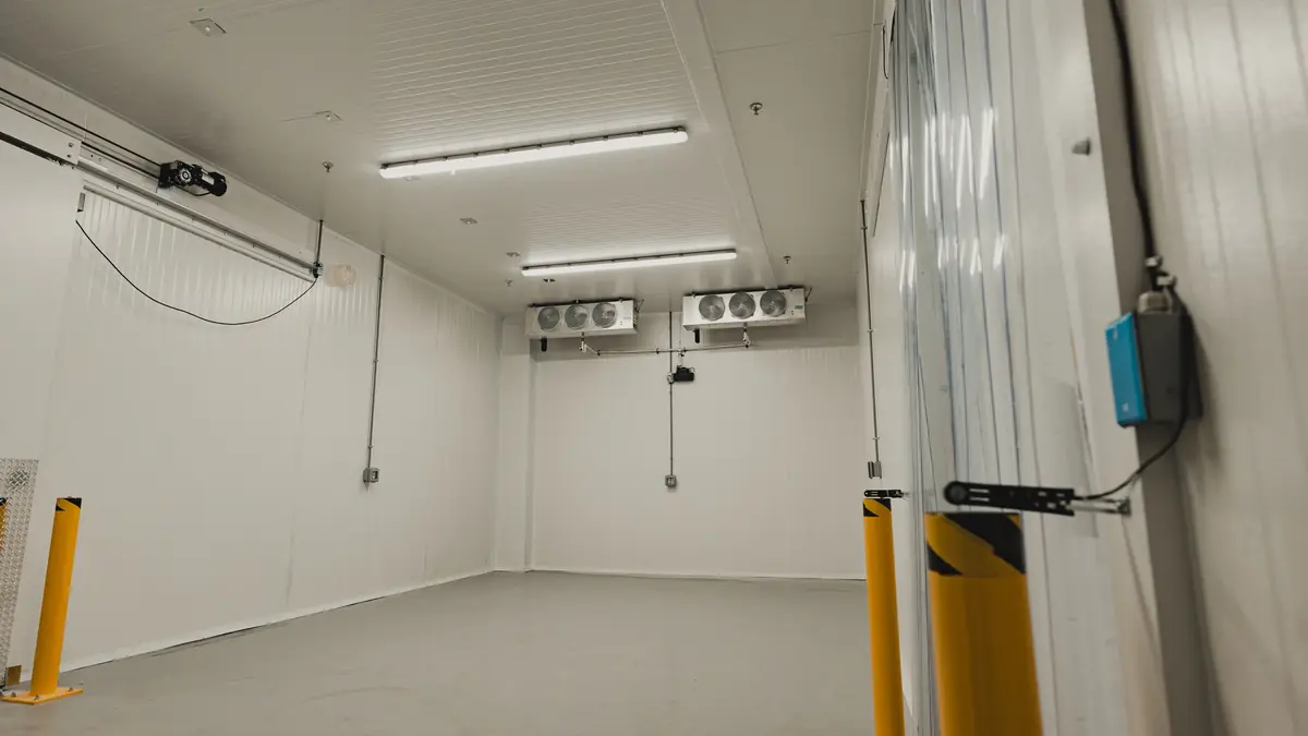 Empty large walk-in freezer built by WFE for a school food supplier in Ontario, with two KeepRite ceiling evaporators and yellow safety bollards at the sliding door