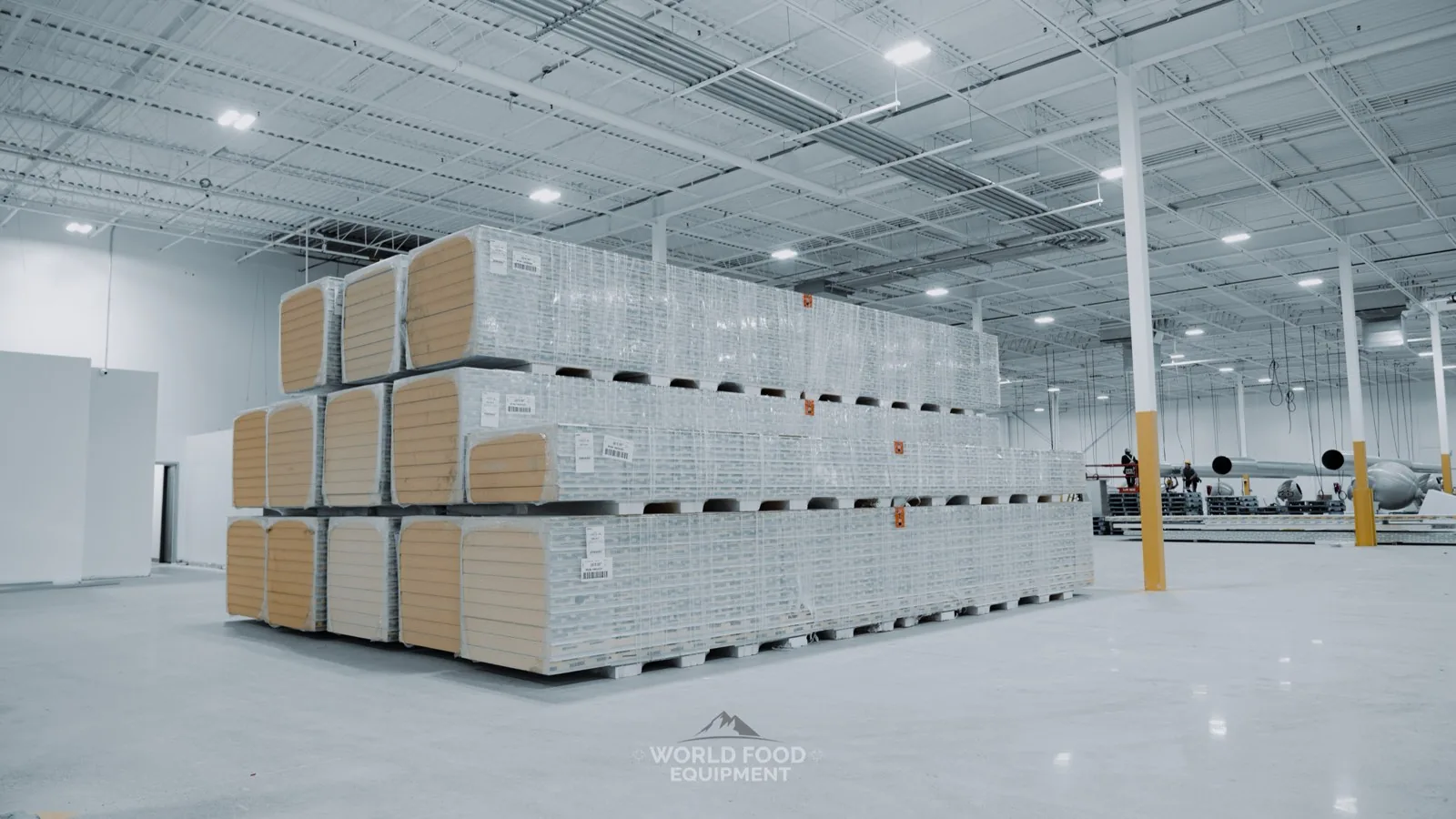 Three tiers of shrink-wrapped insulated freezer panel pallets staged on a polished concrete floor inside a large Ontario warehouse before a World Food Equipment cold storage install
