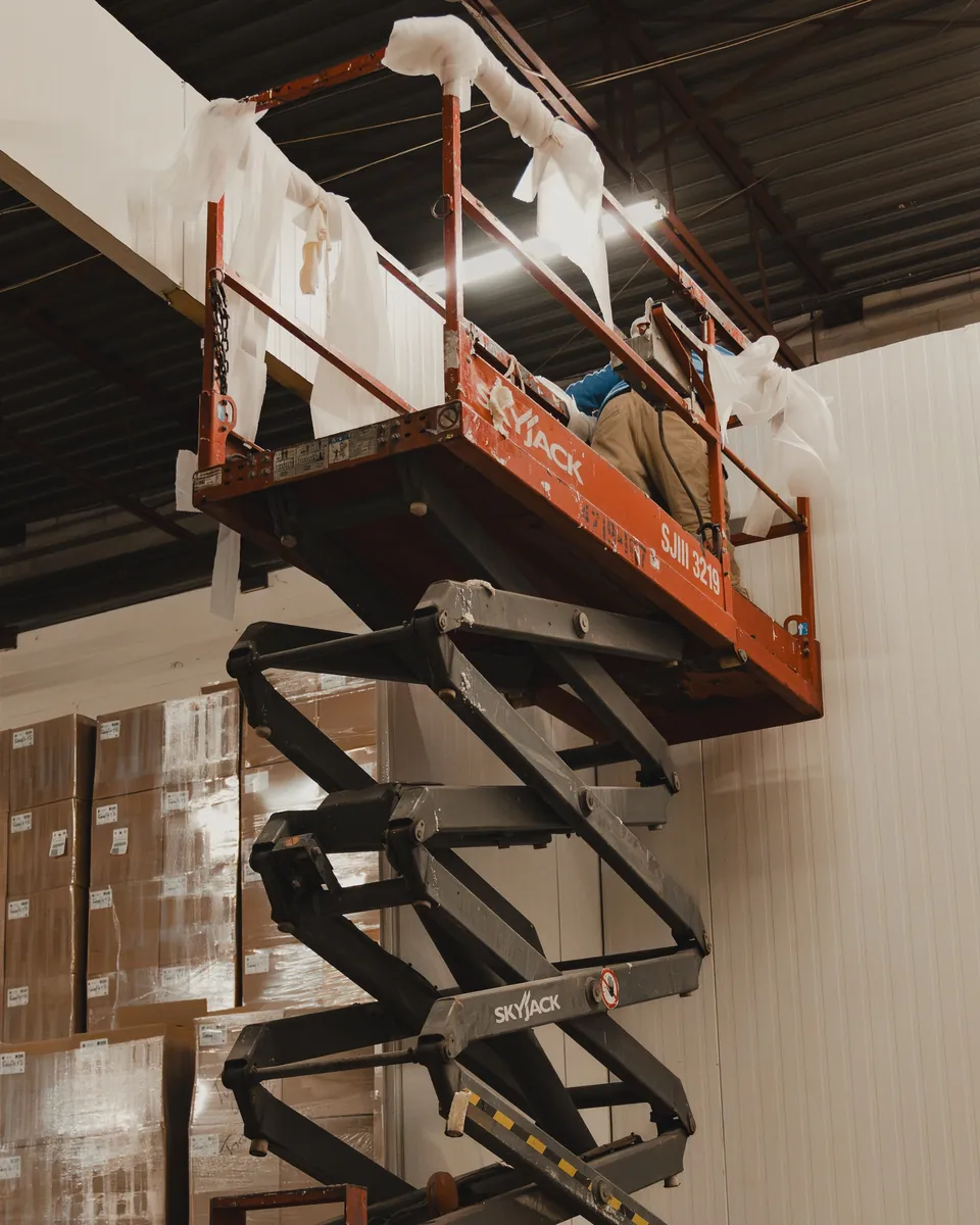 WFE installer on a scissor lift sealing the top of tall white insulated panel walls inside an operating Ontario warehouse during the SKOR Crestlawn freezer build